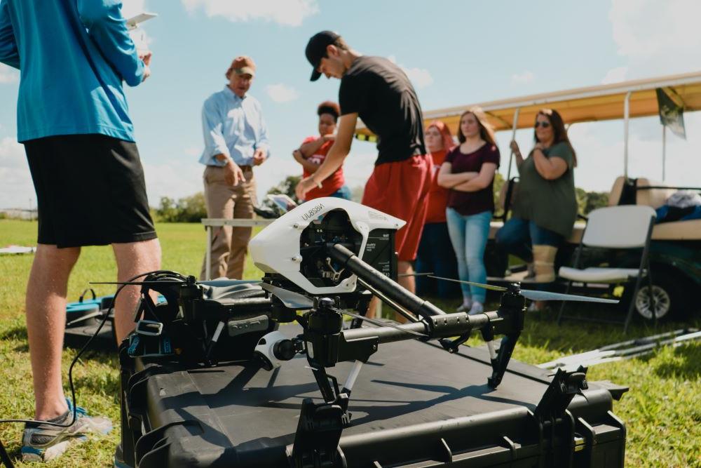 航空专业的学生和一名教师在室外用无人机在一片绿地上工作